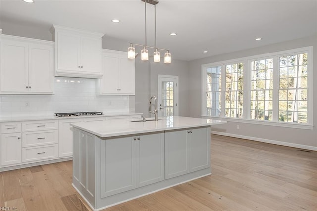 kitchen featuring pendant lighting, white cabinetry, a kitchen island with sink, and sink