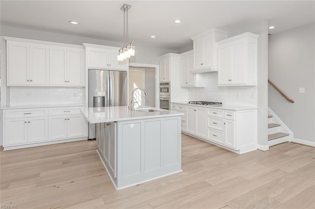 kitchen featuring appliances with stainless steel finishes, decorative light fixtures, sink, white cabinets, and light hardwood / wood-style floors