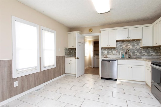 kitchen featuring sink, appliances with stainless steel finishes, white cabinetry, decorative backsplash, and wood walls