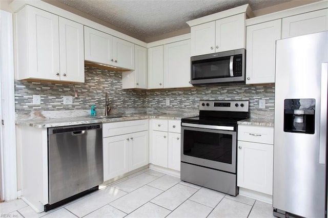 kitchen with appliances with stainless steel finishes, sink, white cabinets, light tile patterned floors, and a textured ceiling