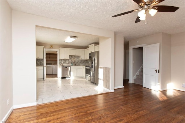 kitchen featuring white cabinetry, appliances with stainless steel finishes, washer and clothes dryer, light hardwood / wood-style floors, and decorative backsplash