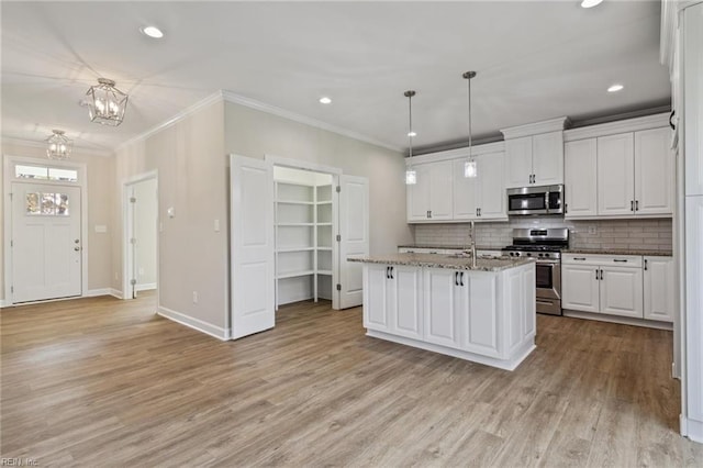 kitchen with appliances with stainless steel finishes, an island with sink, hanging light fixtures, and white cabinets