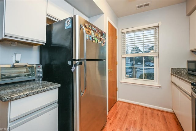 kitchen featuring white cabinetry, light hardwood / wood-style floors, dark stone countertops, and appliances with stainless steel finishes