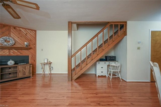 living room with ceiling fan, wooden walls, and light hardwood / wood-style floors