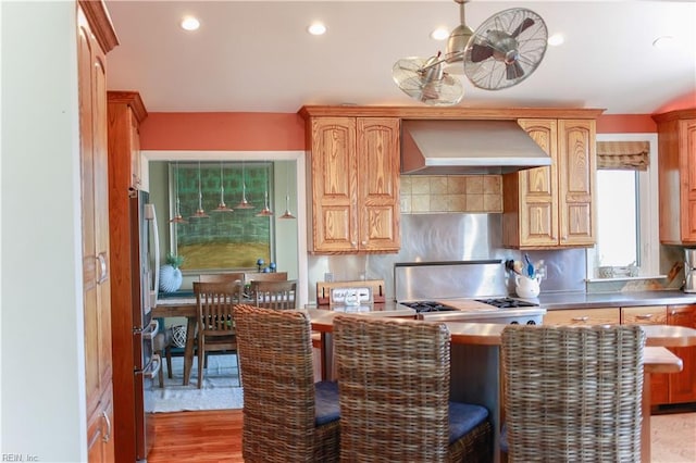 kitchen featuring stainless steel refrigerator, wall chimney exhaust hood, and light wood-type flooring