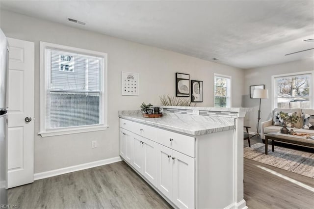 kitchen with white cabinetry, light stone counters, light wood-type flooring, and kitchen peninsula