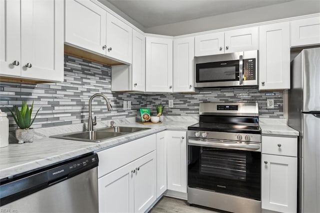 kitchen with sink, white cabinetry, backsplash, stainless steel appliances, and light stone counters