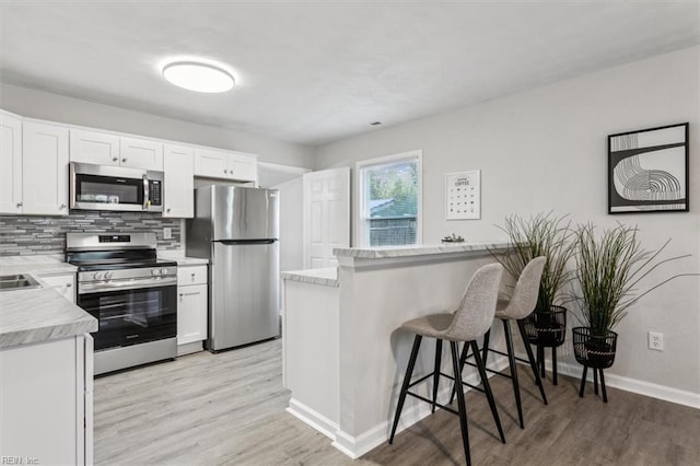 kitchen featuring a breakfast bar area, backsplash, stainless steel appliances, light hardwood / wood-style floors, and white cabinets