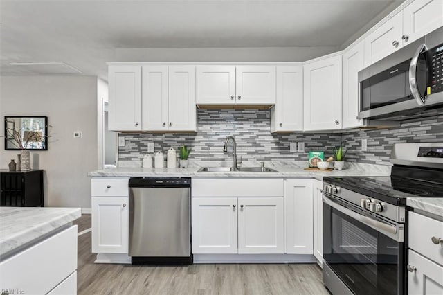 kitchen featuring sink, light stone counters, light wood-type flooring, stainless steel appliances, and white cabinets