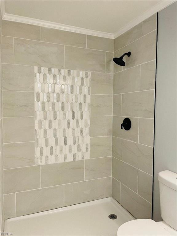 bathroom with ornamental molding, toilet, and tiled shower