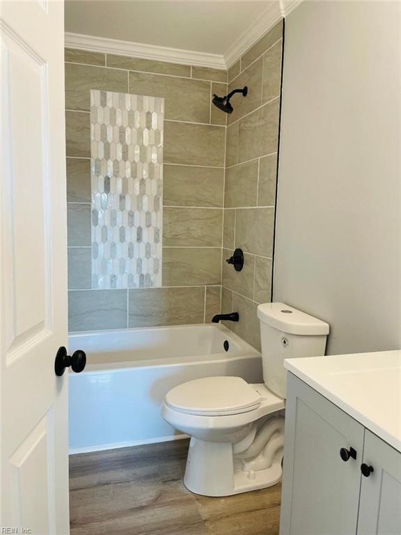 full bathroom with tiled shower / bath, wood-type flooring, vanity, toilet, and crown molding