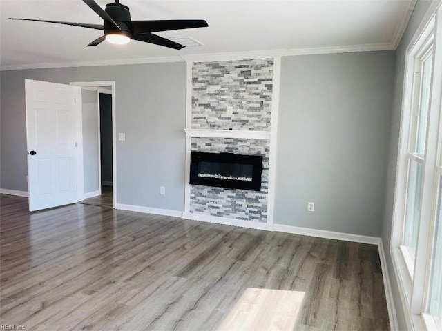 unfurnished living room with ornamental molding, a stone fireplace, wood-type flooring, and ceiling fan