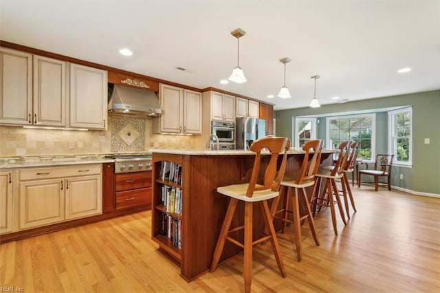 kitchen featuring wall chimney range hood, stainless steel appliances, an island with sink, a kitchen bar, and decorative light fixtures