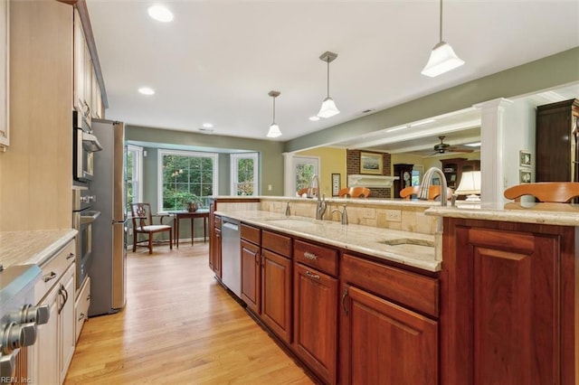 kitchen featuring ornate columns, sink, hanging light fixtures, light hardwood / wood-style floors, and stainless steel appliances