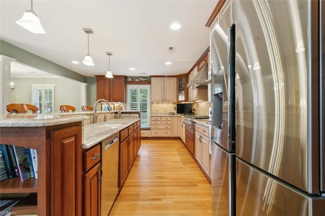 kitchen with pendant lighting, appliances with stainless steel finishes, wall chimney exhaust hood, and light wood-type flooring