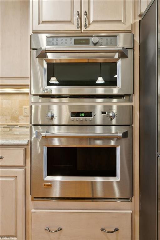 kitchen with light stone counters, appliances with stainless steel finishes, cream cabinets, and decorative backsplash