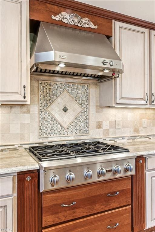 kitchen featuring stainless steel gas cooktop, wall chimney range hood, backsplash, and light stone counters