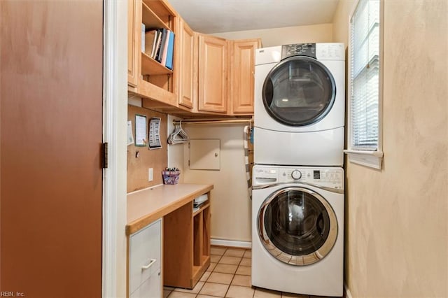 clothes washing area featuring stacked washer and dryer, light tile patterned floors, and cabinets