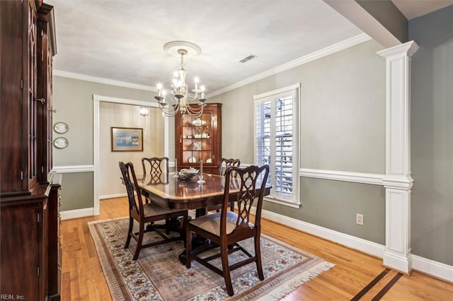 dining area featuring a notable chandelier, light hardwood / wood-style flooring, decorative columns, and ornamental molding