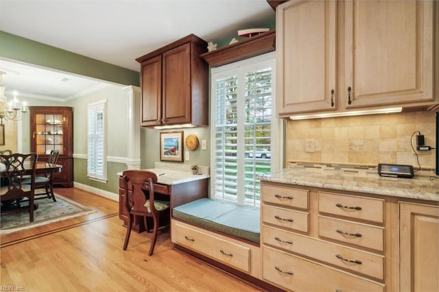 kitchen with tasteful backsplash, an inviting chandelier, crown molding, light stone counters, and light hardwood / wood-style floors