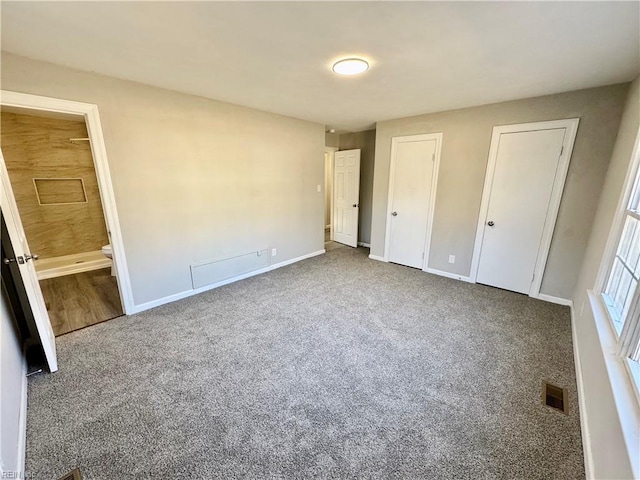 unfurnished bedroom with multiple closets, ensuite bathroom, and carpet flooring