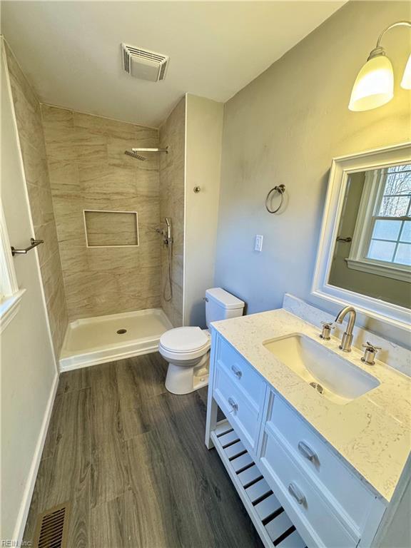 bathroom with a tile shower, vanity, wood-type flooring, and toilet