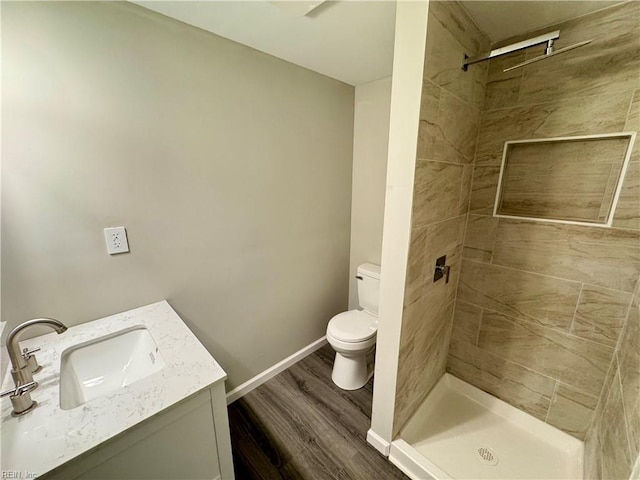 bathroom featuring a tile shower, vanity, hardwood / wood-style floors, and toilet