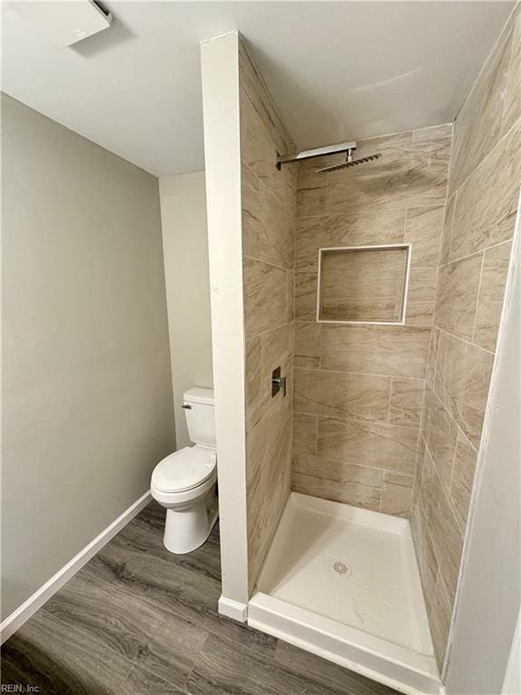 bathroom with hardwood / wood-style flooring, a tile shower, and toilet