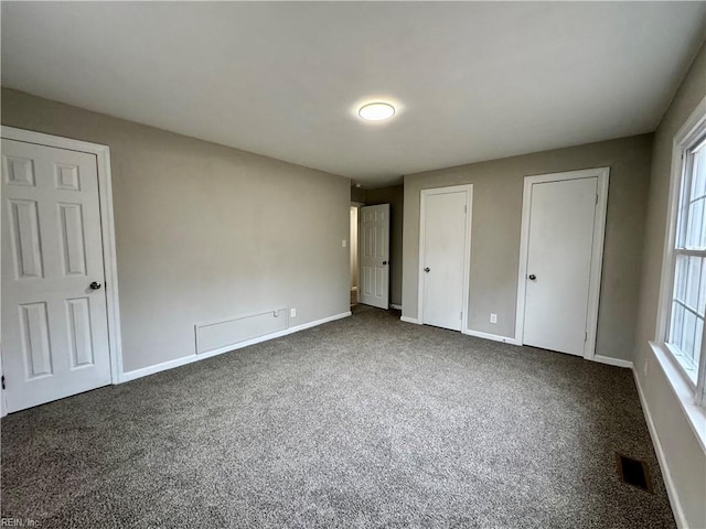 unfurnished bedroom with two closets and dark colored carpet