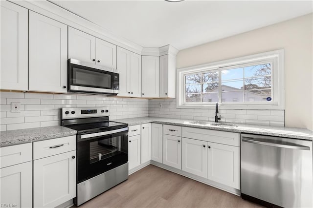 kitchen with appliances with stainless steel finishes, white cabinetry, sink, decorative backsplash, and light stone counters