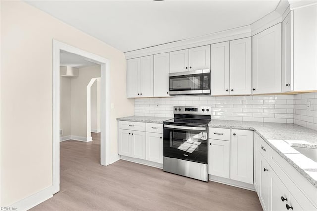 kitchen with stainless steel appliances, white cabinets, light stone counters, and light hardwood / wood-style floors