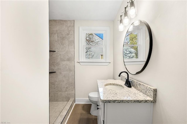 bathroom featuring hardwood / wood-style flooring, vanity, a tile shower, and toilet