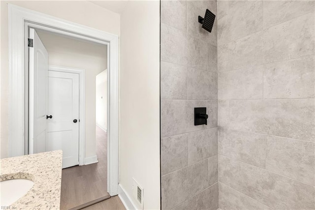 bathroom featuring a tile shower, vanity, and wood-type flooring