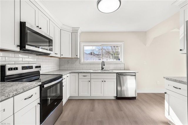 kitchen with appliances with stainless steel finishes, sink, white cabinets, decorative backsplash, and light stone counters