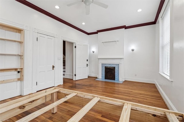 unfurnished living room with crown molding, ceiling fan, hardwood / wood-style floors, and a brick fireplace