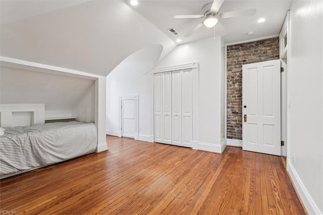 unfurnished bedroom featuring lofted ceiling, light hardwood / wood-style flooring, ceiling fan, brick wall, and a closet