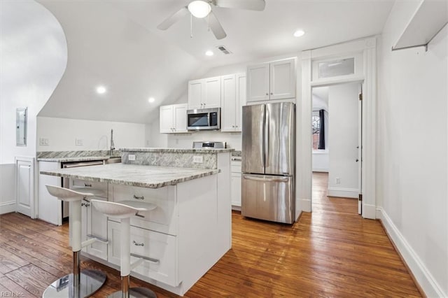 kitchen with a breakfast bar area, white cabinetry, hardwood / wood-style floors, stainless steel appliances, and a center island