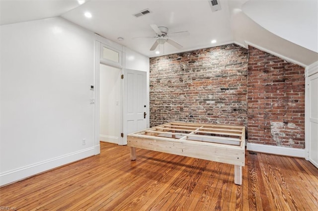 interior space with brick wall, lofted ceiling, and light wood-type flooring