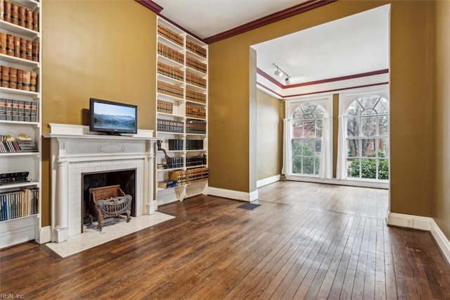 unfurnished living room featuring crown molding, track lighting, built in features, and hardwood / wood-style flooring