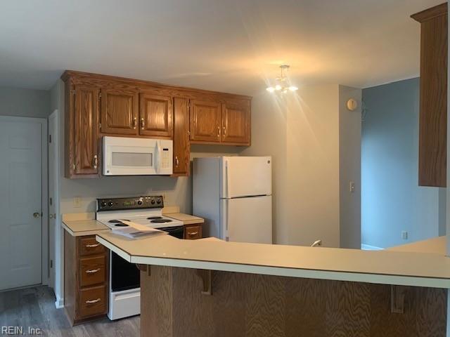 kitchen with a kitchen breakfast bar, dark hardwood / wood-style flooring, kitchen peninsula, a notable chandelier, and white appliances