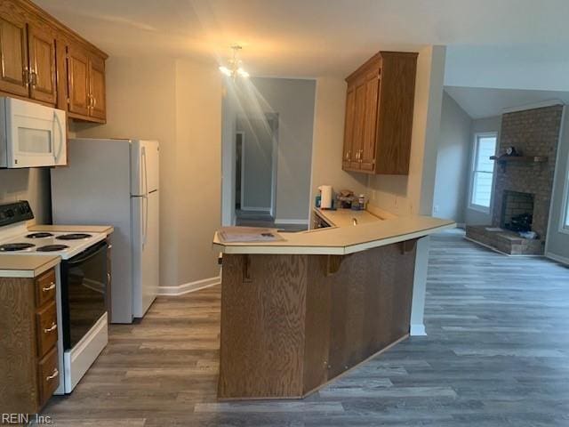 kitchen featuring range with electric cooktop, a kitchen breakfast bar, dark hardwood / wood-style flooring, a brick fireplace, and kitchen peninsula