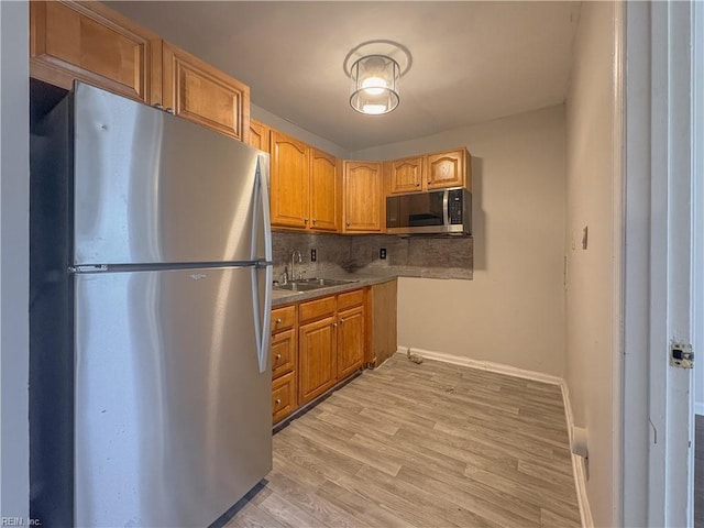 kitchen with tasteful backsplash, appliances with stainless steel finishes, sink, and light wood-type flooring