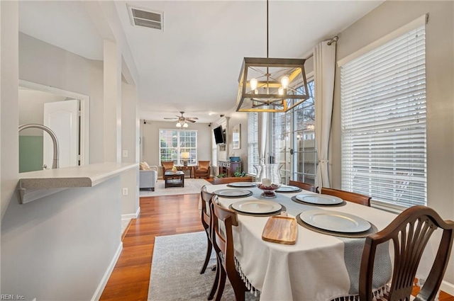 dining space with ceiling fan with notable chandelier and hardwood / wood-style floors