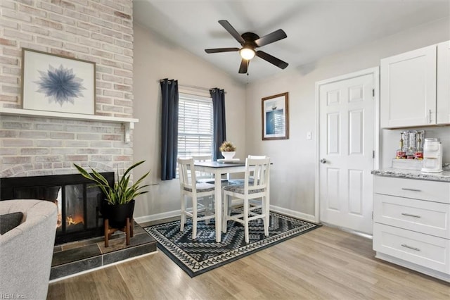 dining area featuring lofted ceiling, a brick fireplace, light hardwood / wood-style floors, and ceiling fan