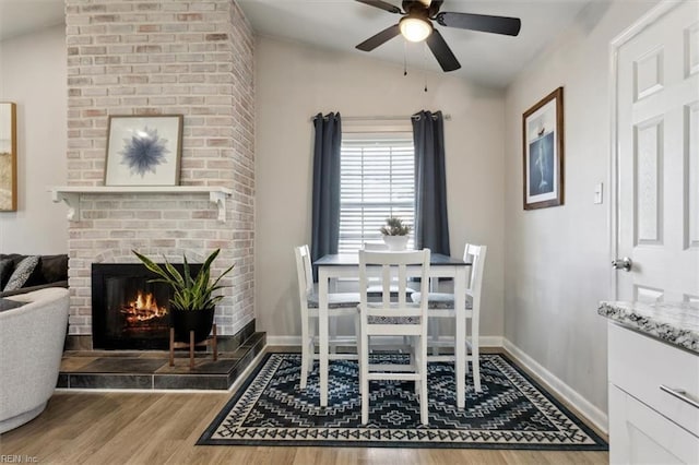 dining space with ceiling fan, lofted ceiling, hardwood / wood-style floors, and a fireplace