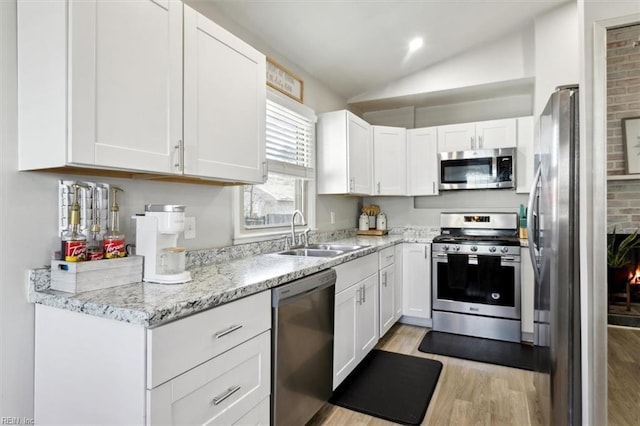 kitchen with lofted ceiling, sink, appliances with stainless steel finishes, light stone countertops, and white cabinets