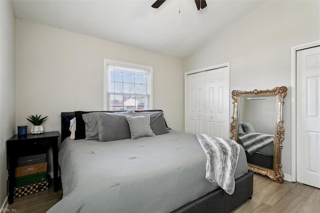 bedroom with multiple closets, lofted ceiling, hardwood / wood-style floors, and ceiling fan