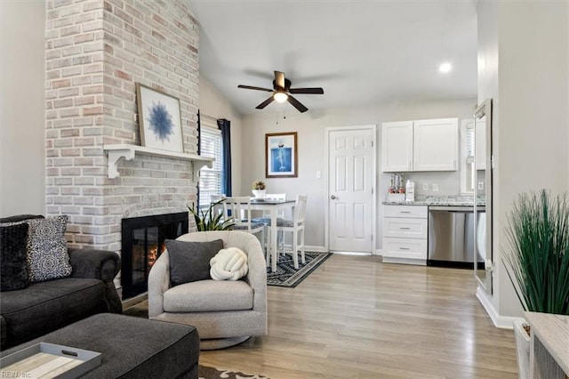 living room featuring ceiling fan, lofted ceiling, a fireplace, and light wood-type flooring