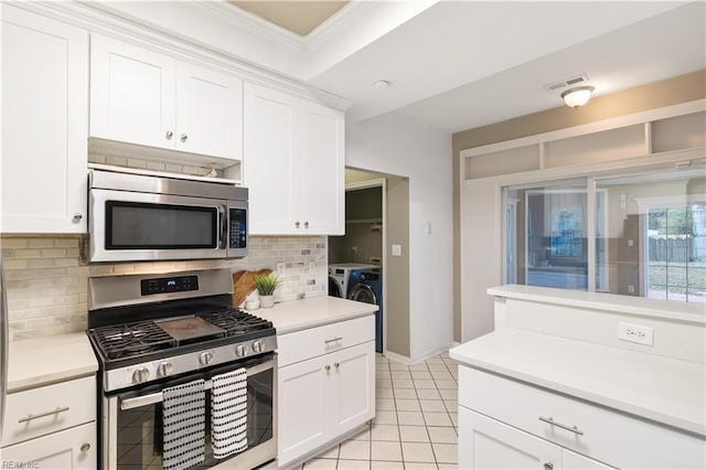 kitchen with tasteful backsplash, white cabinets, light tile patterned floors, stainless steel appliances, and washing machine and dryer