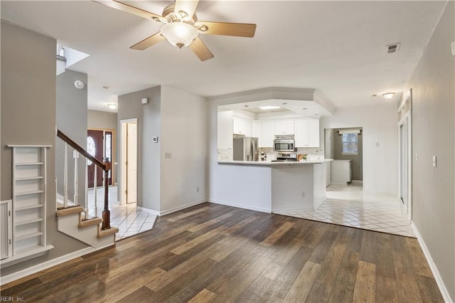 kitchen with white cabinetry, wood-type flooring, kitchen peninsula, stainless steel appliances, and decorative backsplash